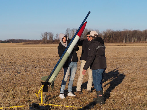 Akronauts Adam McElfresh (left) and Matthew Reppa, along with Chris Pearson, the team’s mentor, load their rocket onto the launch rail, which keeps the rocket going straight as it initially builds up speed. This test launch was held at the National Association of Rocketry field located in Amherst.