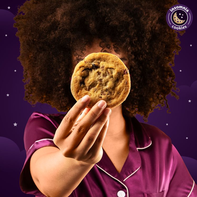 Woman in pajamas holding an Insomnia cookie. 