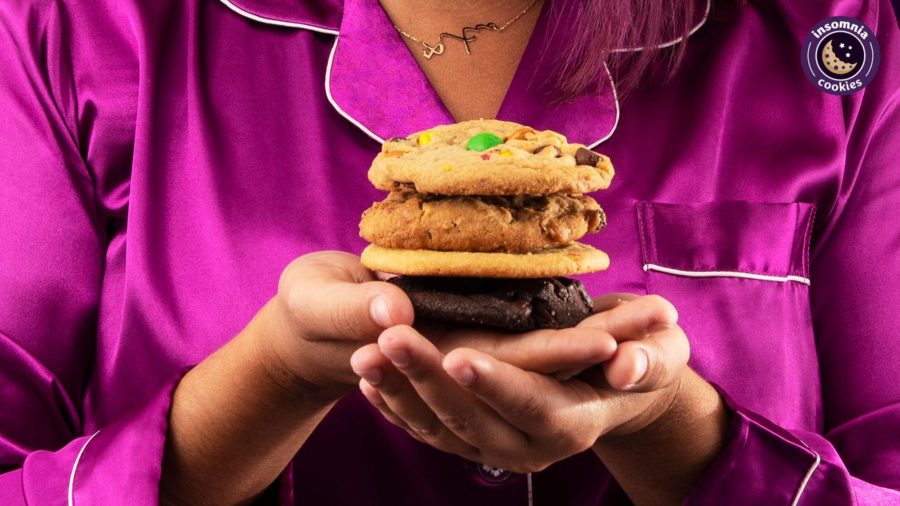 Woman in pink pajamas holding stack of Insomnia Cookies. 
