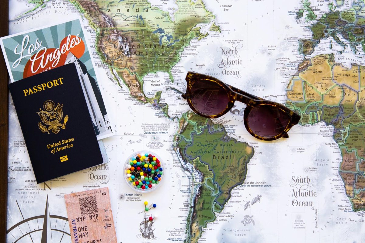 Map with a passport, sunglasses, pins, and plane ticket (on Pexels).